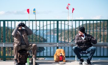 Pontus Berglund (L) looks at birds into his binoculars as he sits on the Swedish side while his brother Ola sits on the Norwegian side of the old bridge of Svinesund and the new Svinesund Bridge is seen in the background, in Svinesund, Norway and Sweden, on May 1, 2021. They haven
