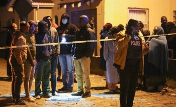 Los miembros de la comunidad y la familia esperan noticias fuera de un pub del municipio mientras un oficial de policía habla por teléfono en la ciudad de East London, en el sur de Sudáfrica