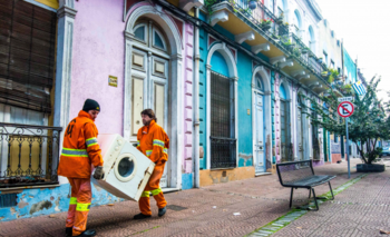 Dos funcionarios de la Intendencia de Montevideo retiran un electrodoméstico de una casa.