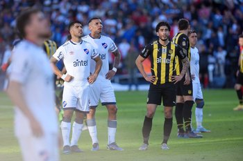 Los jugadores de Nacional y Peñarol observan mientras el partido está detenido por el enfrentamiento entre hinchas en la tribuna