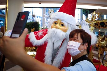 Un hombre disfrazado de Papá Noel posa para fotografías con un hombre con tapabocas en un centro comercial en Bangkok, Tailandia.