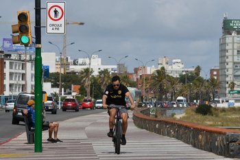 Ciclista en la Rambla de Montevideo, al lado de un cartel de "circule a pie"
