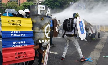 Manifestantes sostienen un cartel con nombres de personas muertas durante las recientes protestas en Venezuela mientras son rociados por un camión hidrante, el pasado 10 de mayo. 